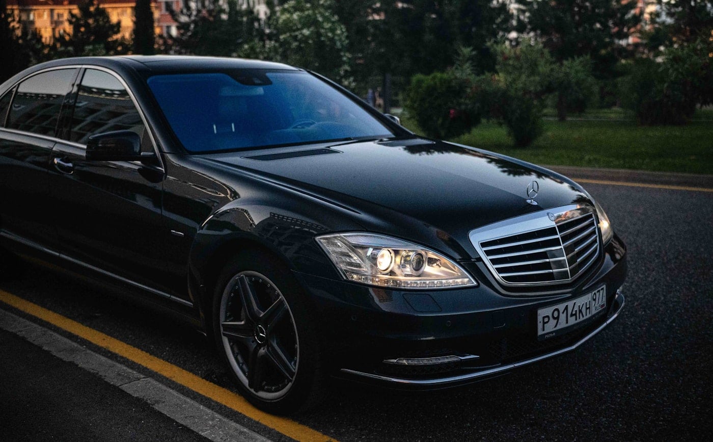A black luxury sedan on a tree-lined road